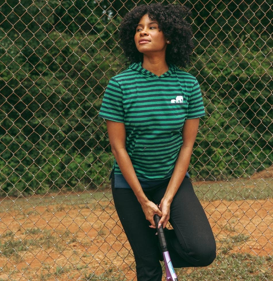 Woman in a green striped tee kneeling beside a chain link fence, tennis racket in hand
